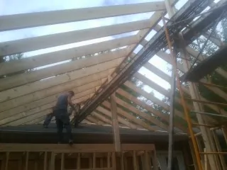 Rafters going up over a new addition with a worker on the wall in Little Falls