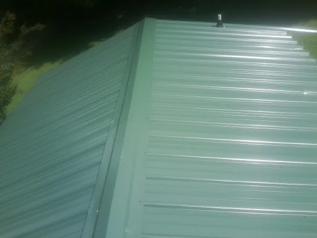 New green metal panels meeting at the ridge of a roof — Flat Roof Repair work by our crew in Little Falls