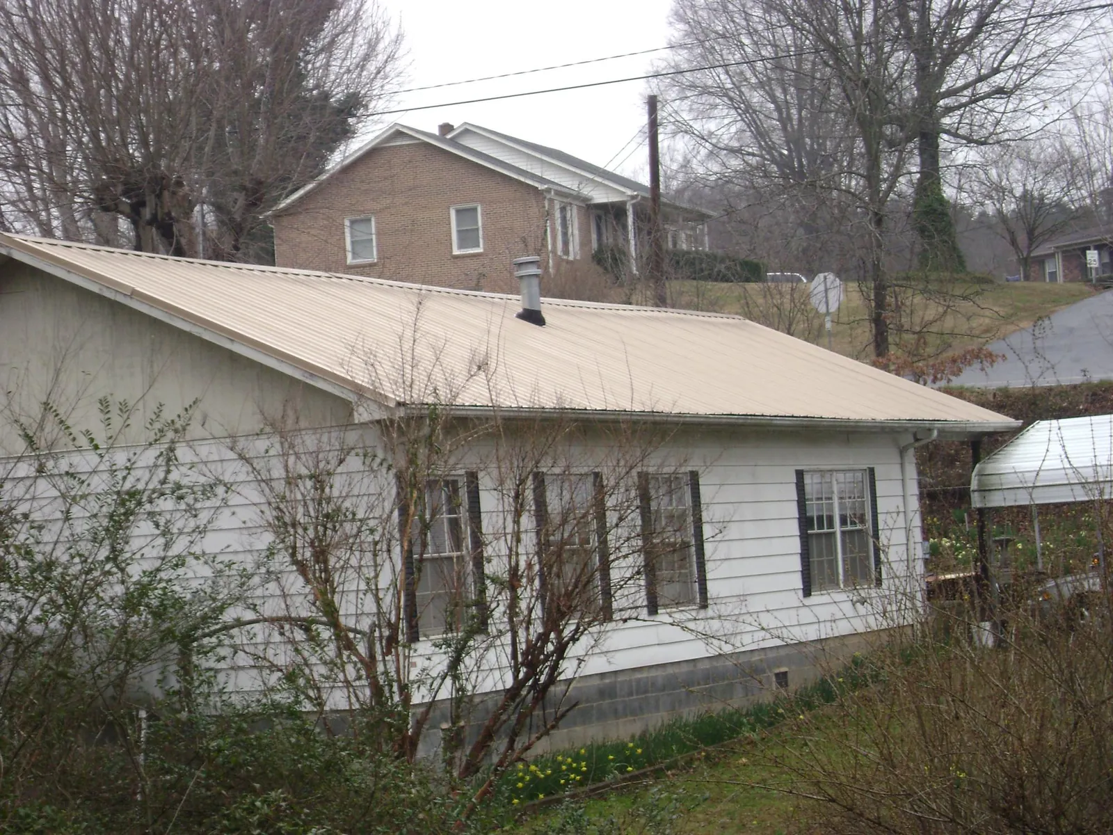 Tan metal roof on a white sided house set into a hillside — Commercial Roofing by Roofing Brothers in Little Falls