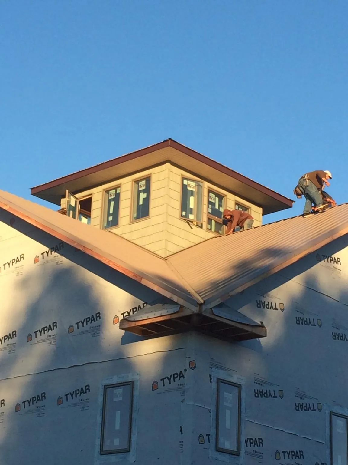 Roofers working around a rooftop cupola on a new metal roof at sunset — Roof Waterproofing in Little Falls by Roofing Brothers